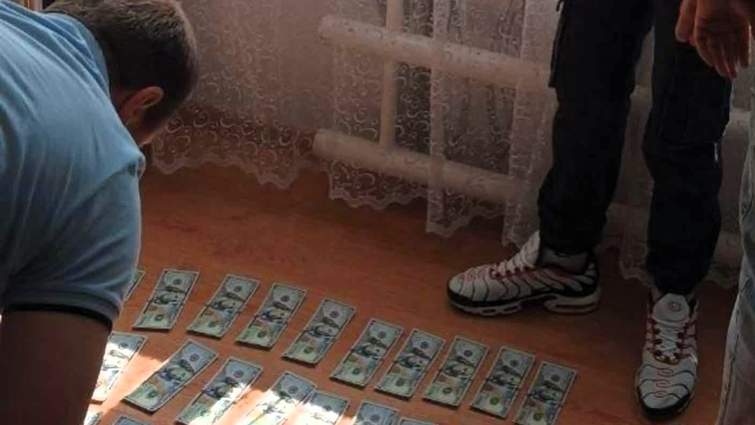 Чоловік розглядає розкладені на підлозі пачки гривень, викрадені у колишньої вчительки на Франківщині