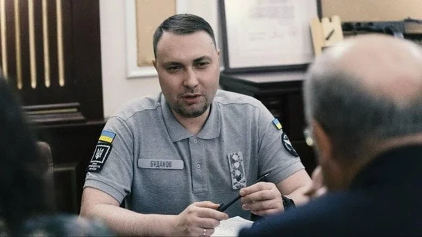 Кирило Буданов у сірій сорочці з нашивками сидить за столом і говорить