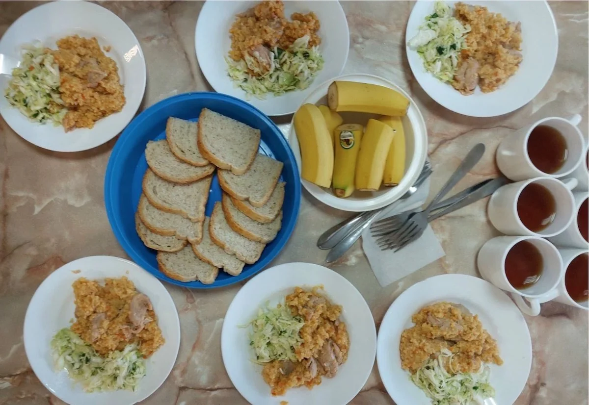 Тарілки з кашею мясом і капустою хліб банани чашки чаю на мармуровому столі