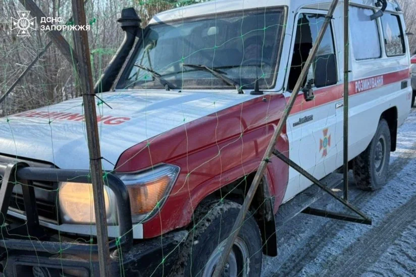 Біло-червоний автомобіль ДСНС для розмінування за зеленою сіткою на снігу